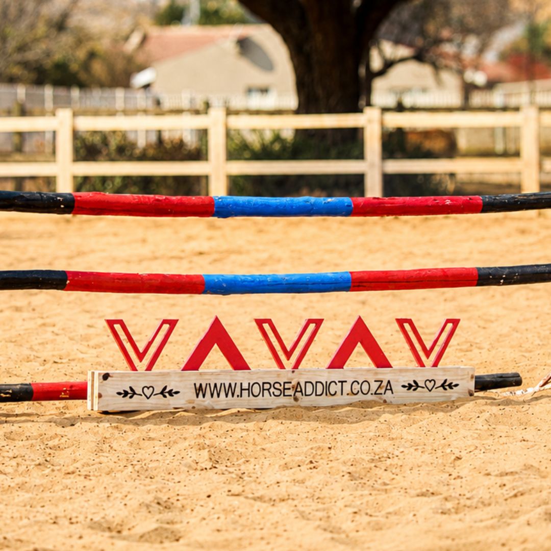 Blush pink chevron wooden jump filler positioned beneath red blue and black show jumping poles in a sand arena