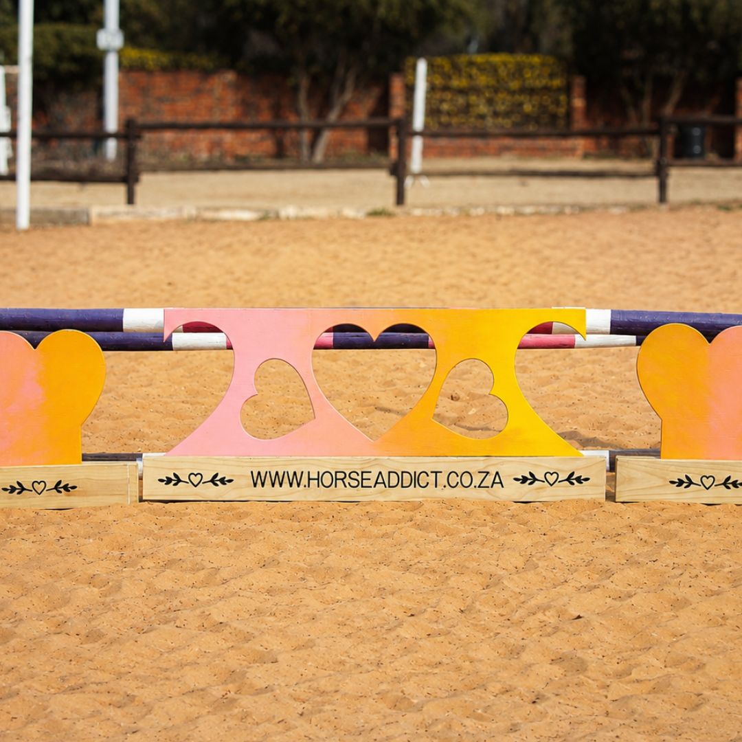 Close view of pink yellow and orange wooden heart jump fillers with heart cut-outs and custom pine bases